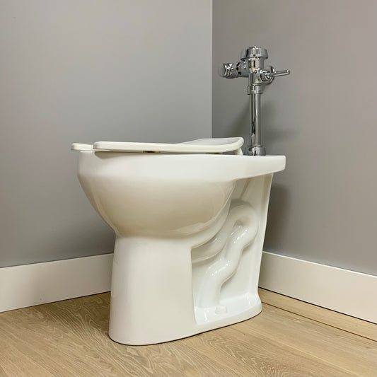 A white, extra tall elongated commercial toilet bowl with an open lid, mounted on the floor against a gray wall.